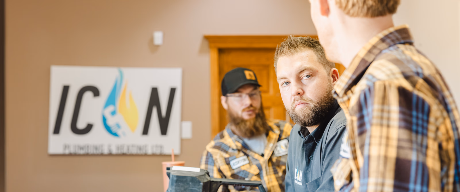 Three professional plumbers in work attire discuss a project inside the Icon Plumbing & Heating Ltd. office.